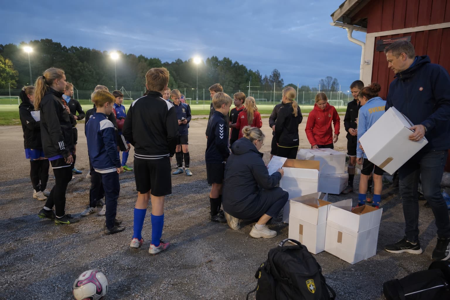 Förening samlas vid planen i skymningen och delar upp lådorna de sålt